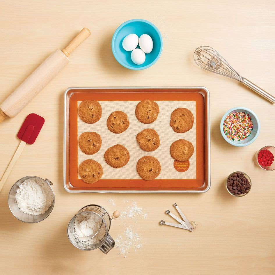 Baking tray with cookies, rolling pin, and various baking ingredients on a wooden surface