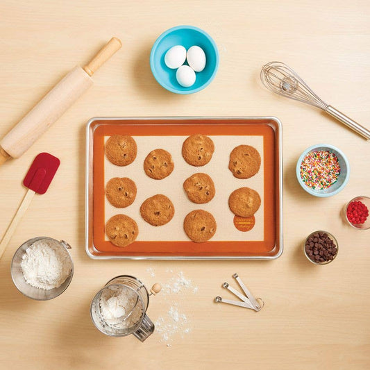 Baking tray with cookies, rolling pin, and various baking ingredients on a wooden surface
