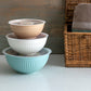 Stack of three mixing bowls with lids on a neutral background