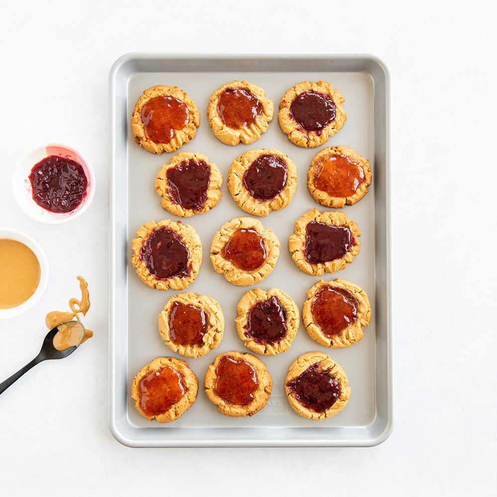 Biscuits with jam on a baking tray, surrounded by peanut butter and jelly.