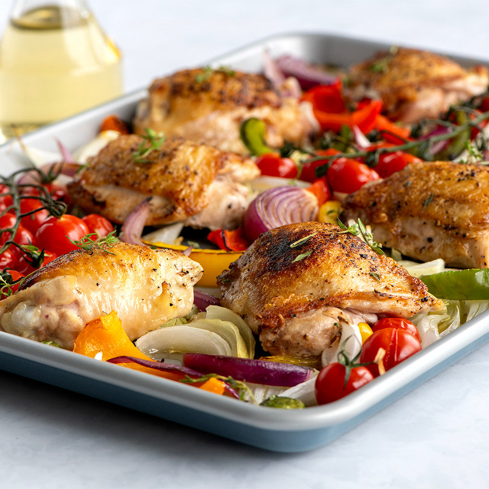 Roasted chicken with vegetables on a white plate with a glass of white wine in the background.