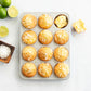 Muffin tin with coconut muffins on a white surface with limes and coconut flakes.
