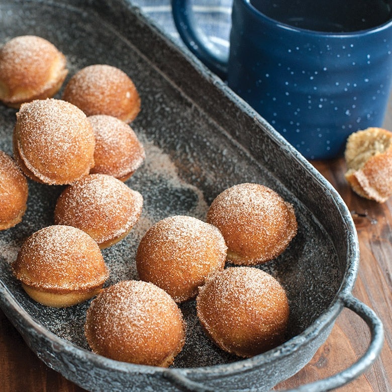 Sugared donut holes in a baking dish with a blue mug in the background