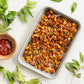 Tray of roasted mixed nuts with a small bowl of seasoning on a white background