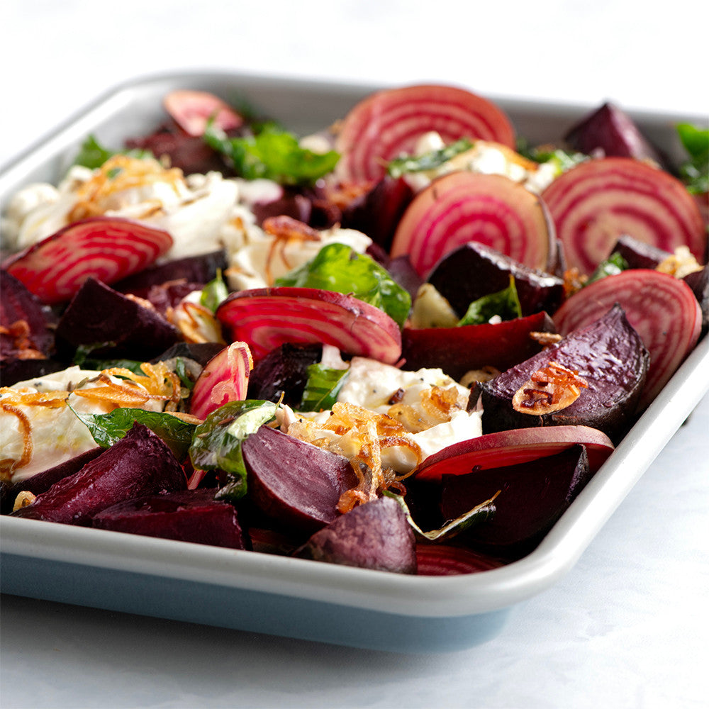 Beet salad with feta cheese and herbs in a white dish on a light background