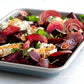Beet salad with feta cheese and herbs in a white dish on a light background