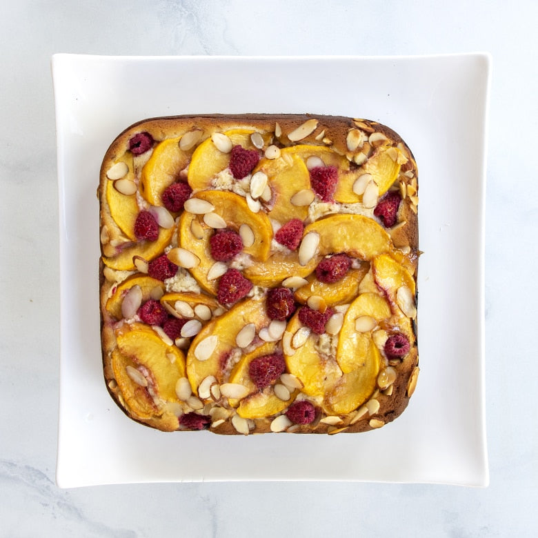 Square baked good with peaches and raspberries on a white plate