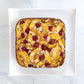 Square baked good with peaches and raspberries on a white plate