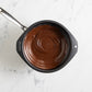 Melted chocolate in a black measuring cup on a marble surface