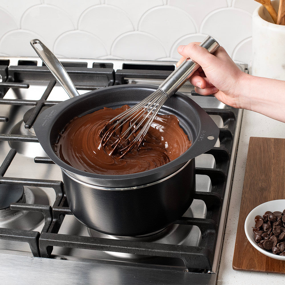 Person stirring chocolate in a pot on a stove with a whisk