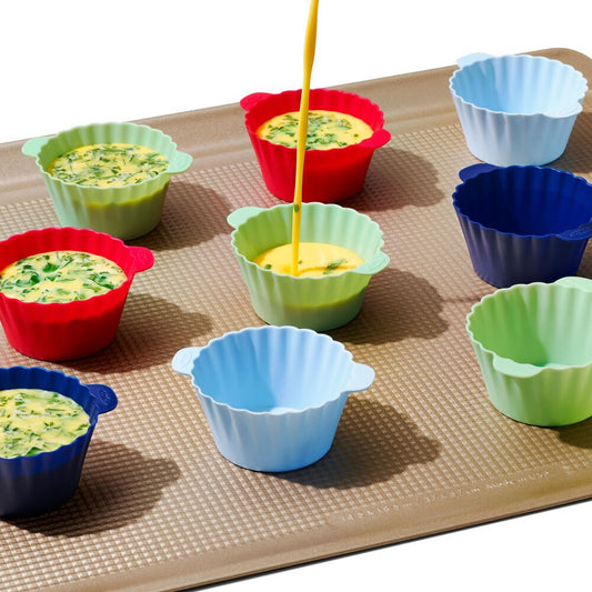 Colorful silicone baking cups on a baking sheet with eggs being poured into them.