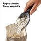 Hand using a black measuring scoop to pour flour into a paper bag with text indicating approximate 1-cup capacity.