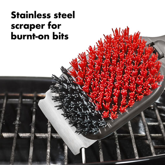 Stainless steel scrubber with red bristles on a grill