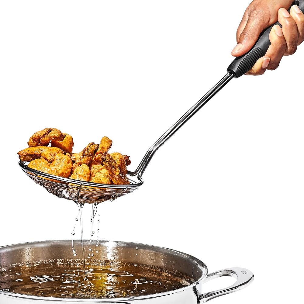 Fried chicken being drained of oil using a slotted spoon over a frying pan.