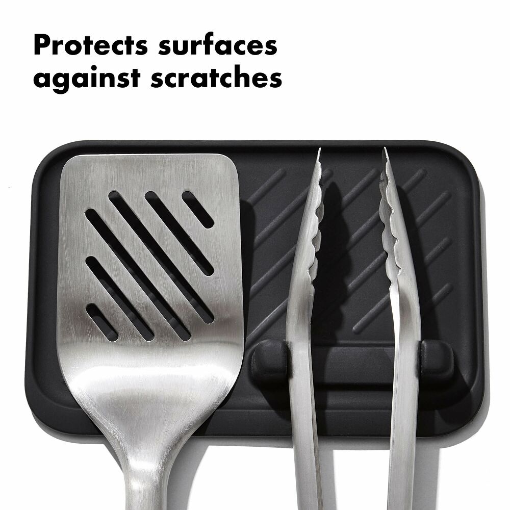 Set of kitchen utensils with a black mat underneath, text 'Protects surfaces against scratches'.