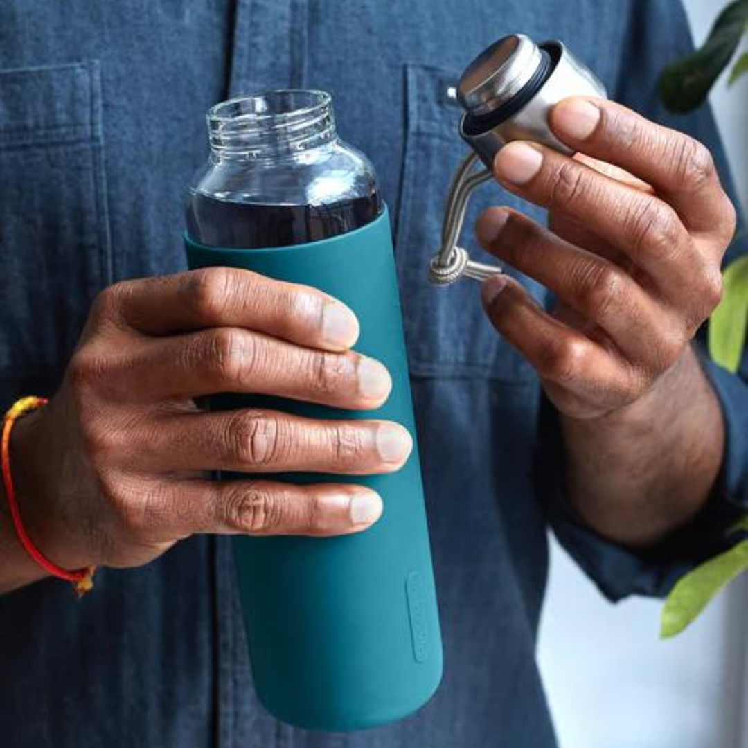 Glass water bottle from black and blum with an aqua ocean blue silicone sleeve being held