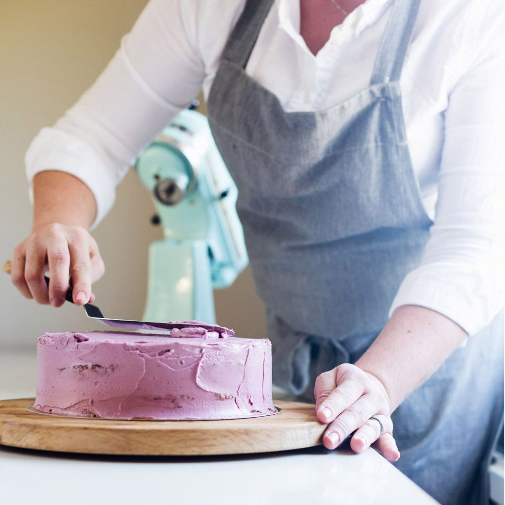 Person frosting a cake with a spatula on a wooden board.