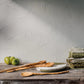 Wooden table with kitchen utensils and green apples against a textured wall.