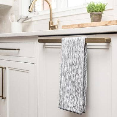 Kitchen cabinet with a towel hanging on a wooden bar, sink and potted plant in the background.