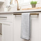 Kitchen cabinet with a towel hanging on a wooden bar, sink and potted plant in the background.