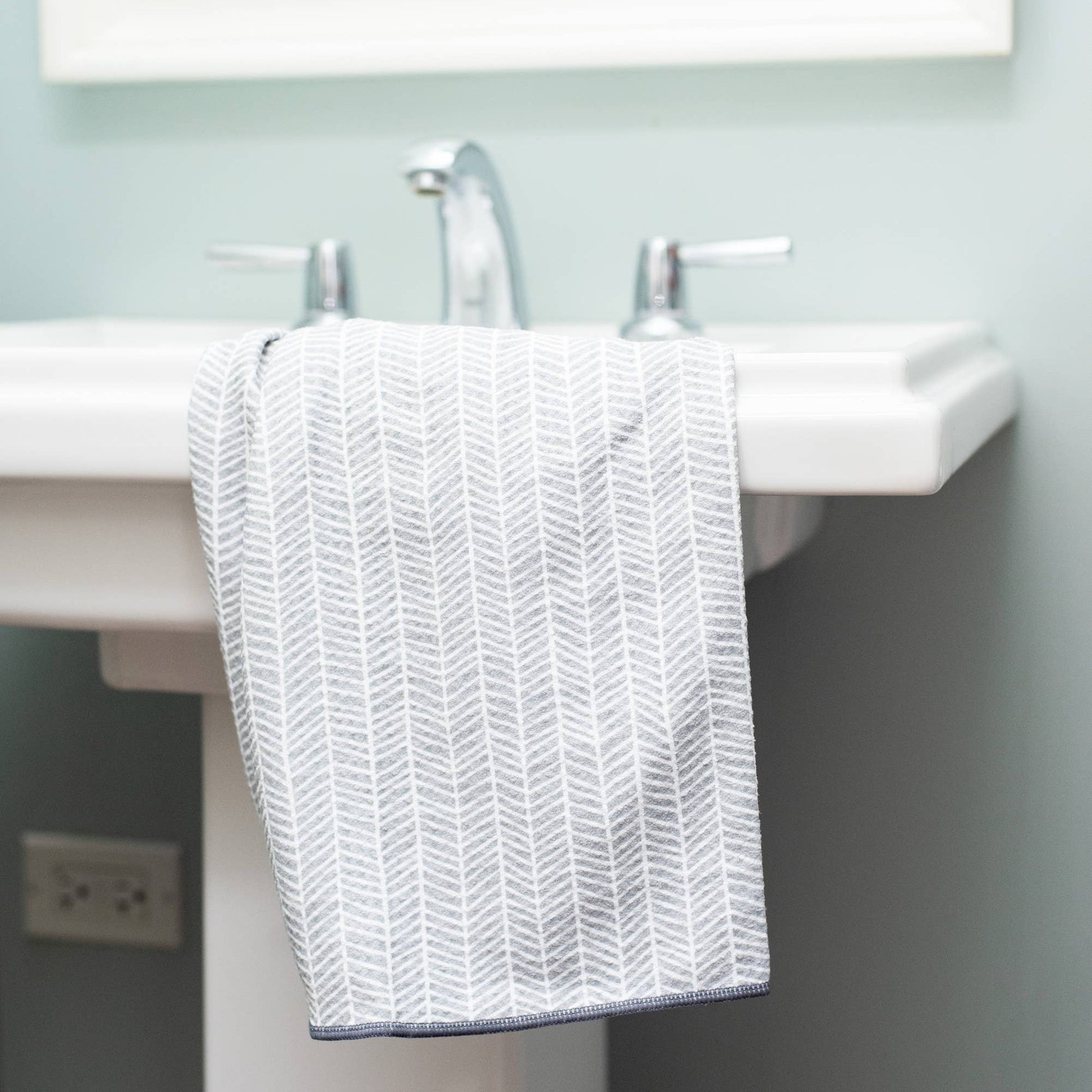 White sink with a patterned towel hanging on it against a light blue wall.
