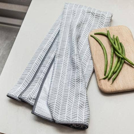 Folded gray and white patterned towel on a marble surface with green beans on a cutting board.
