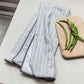 Folded gray and white patterned towel on a marble surface with green beans on a cutting board.