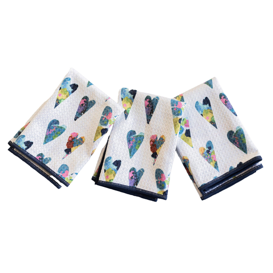 Set of three folded towels with colorful heart pattern on a white background