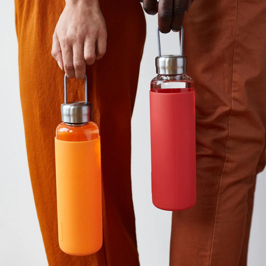 Glass water bottle being held with an orange silicone sleeve