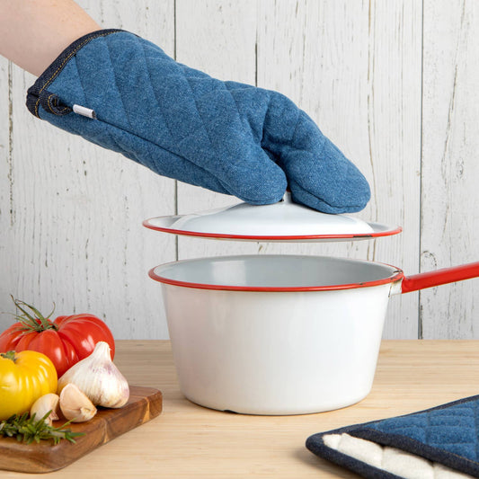White pot with red handle and trim on a wooden surface, with a blue oven mitt lifting the lid.