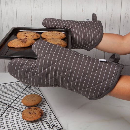 Person wearing striped oven mitts holding a tray of cookies with more cookies on a cooling rack.