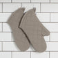 Pair of grey quilted oven mitts on a white tiled wall background