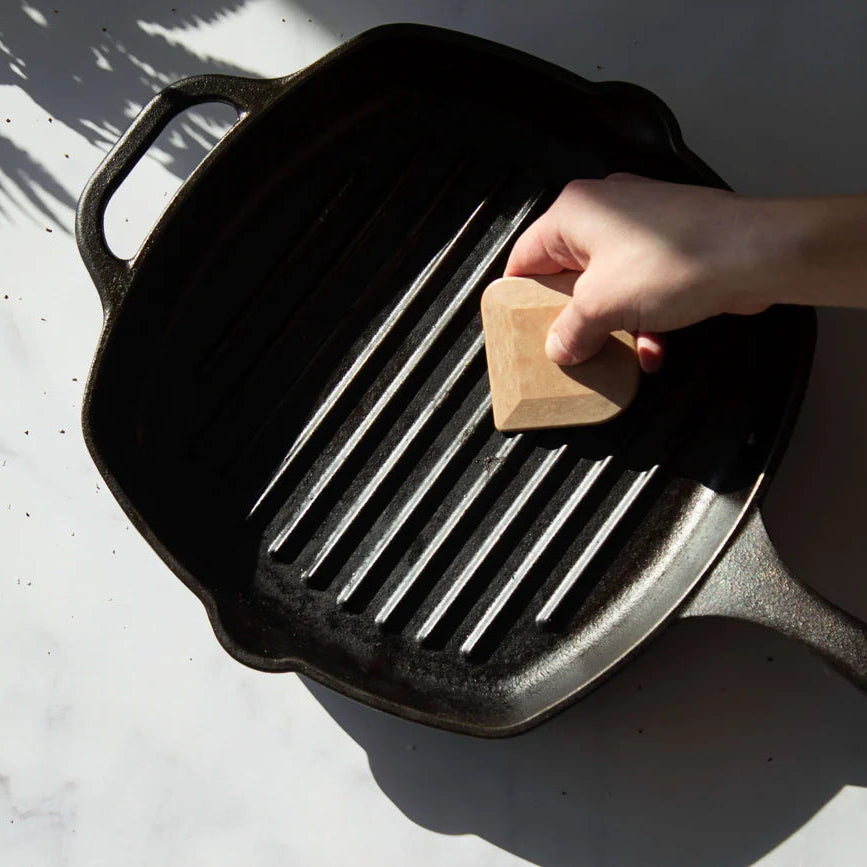 Person using a sponge to clean a black cast iron grill pan on a light background