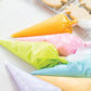 Colorful piping bags filled with icing on a white surface with cookies in the background.