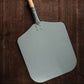 Gray pizza peel with wooden handle on a wooden background
