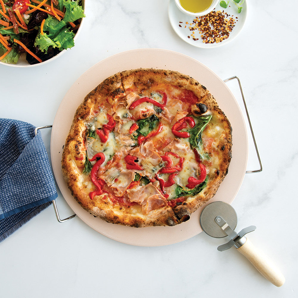 Pizza with red peppers and spinach on a white surface with a pizza cutter.