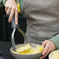 Person using a kitchen tool to mash potatoes in a bowl.