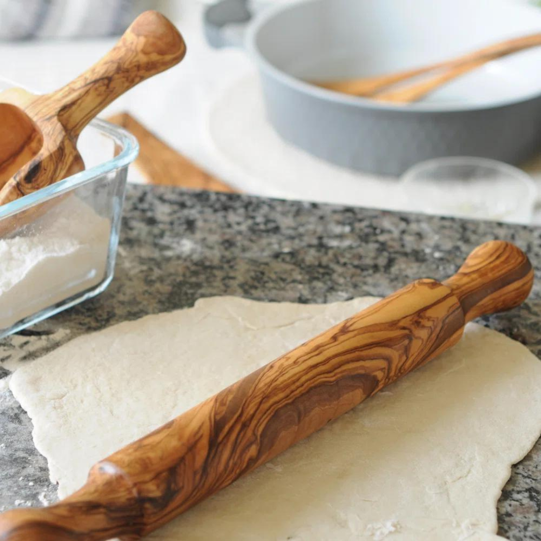 olive wood rolling pin being used on a counter with dough and flower