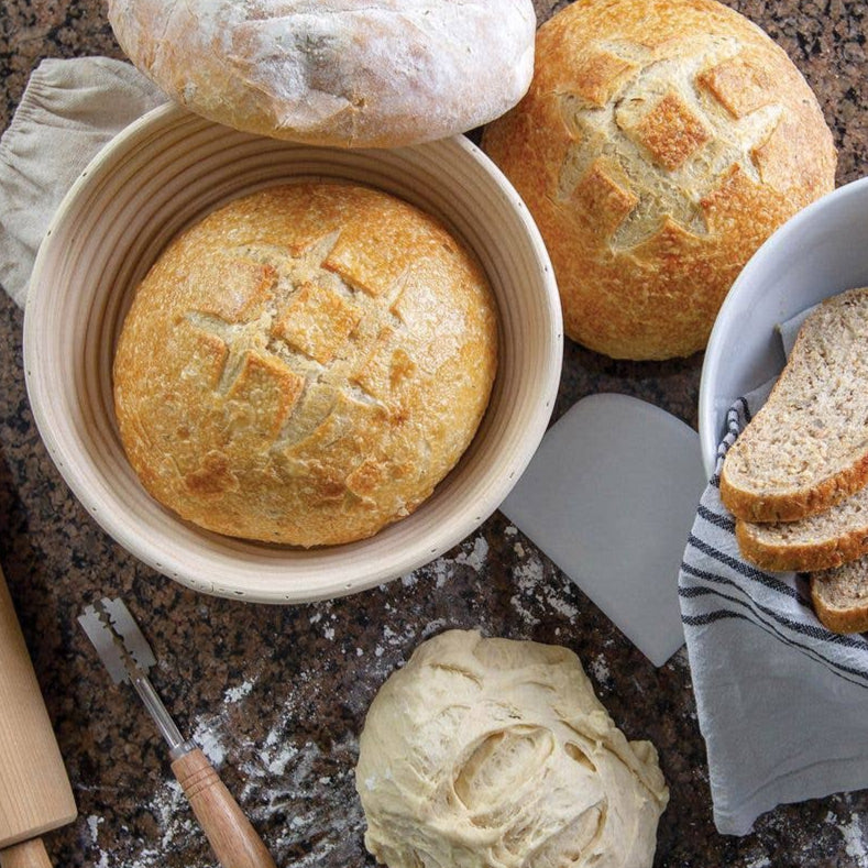Loaves of bread in a basket with a spatula and rolling pin on a countertop.