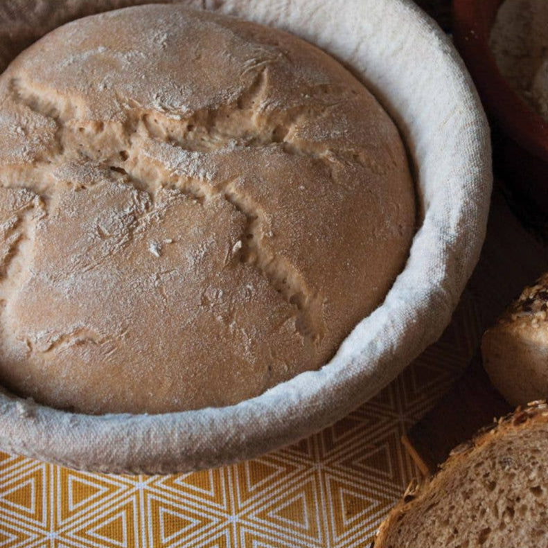 Loaf of bread in a white ceramic dish on a patterned surface