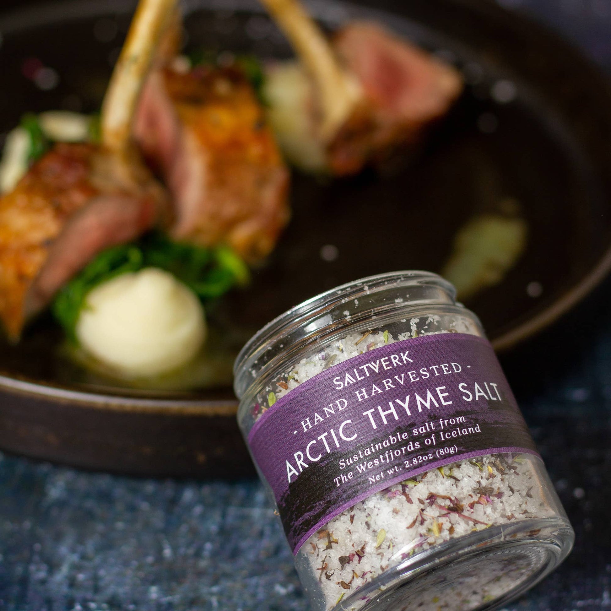 Jar of Saltwerk Arctic Thyme Salt with a plate of food in the background