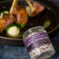 Jar of Saltwerk Arctic Thyme Salt with a plate of food in the background