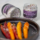 Two jars of Saltverk Arctic Thyme Salt on a white surface with colorful carrots.