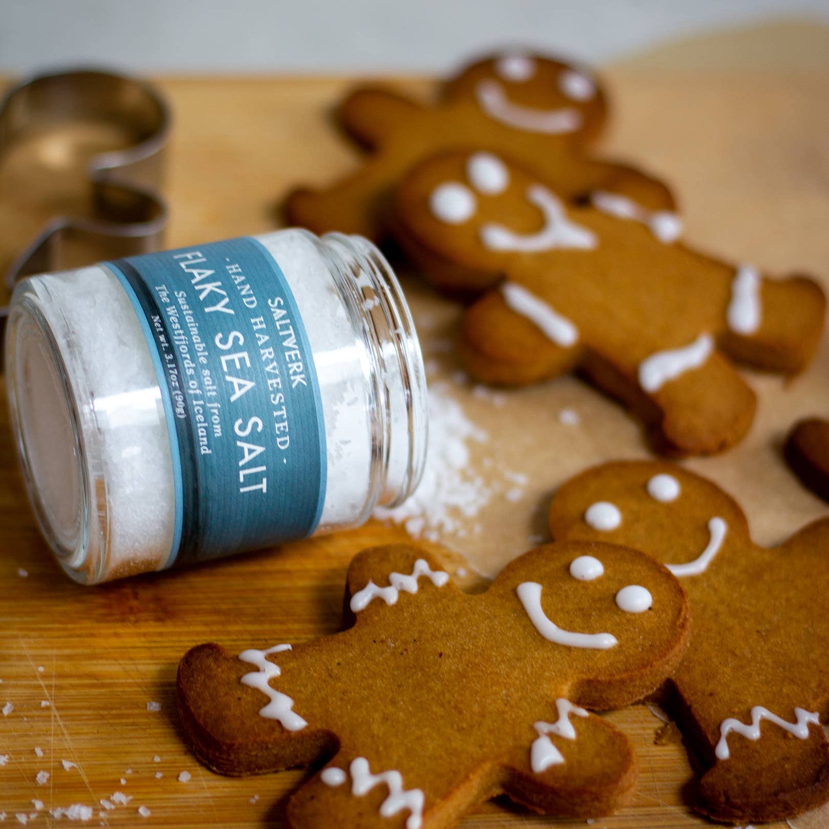 Gingerbread cookies with white icing on a wooden board with a jar of flaky sea salt.