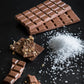 Chocolate bars and pieces with a pile of salt on a dark surface