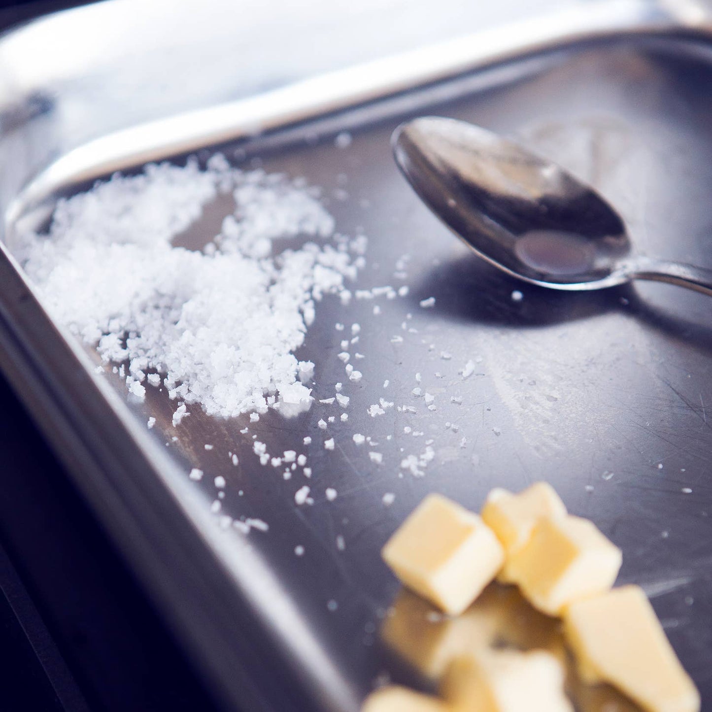 Spoon and salt on a metallic surface with butter cubes nearby