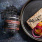 Plated dish with salmon and vegetables next to a jar of Saltwerk Lava Salt on a dark surface.