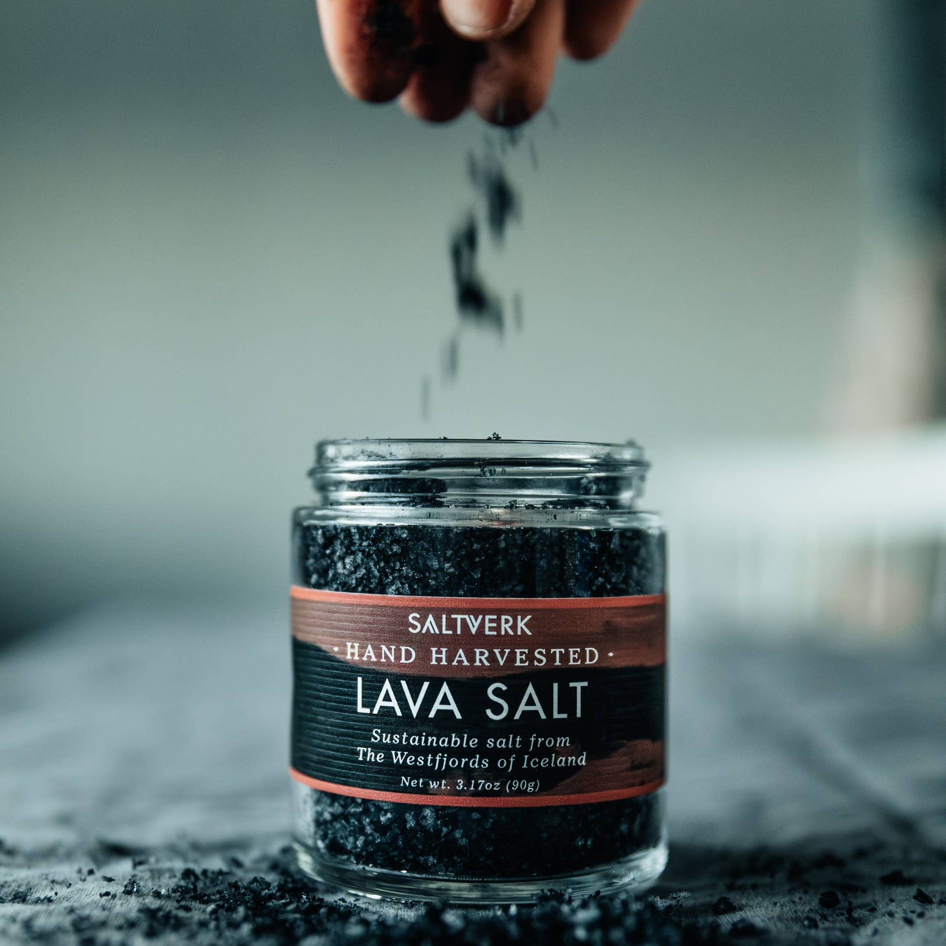 Jar of Saltwerk Lava Salt with hand sprinkling salt over it