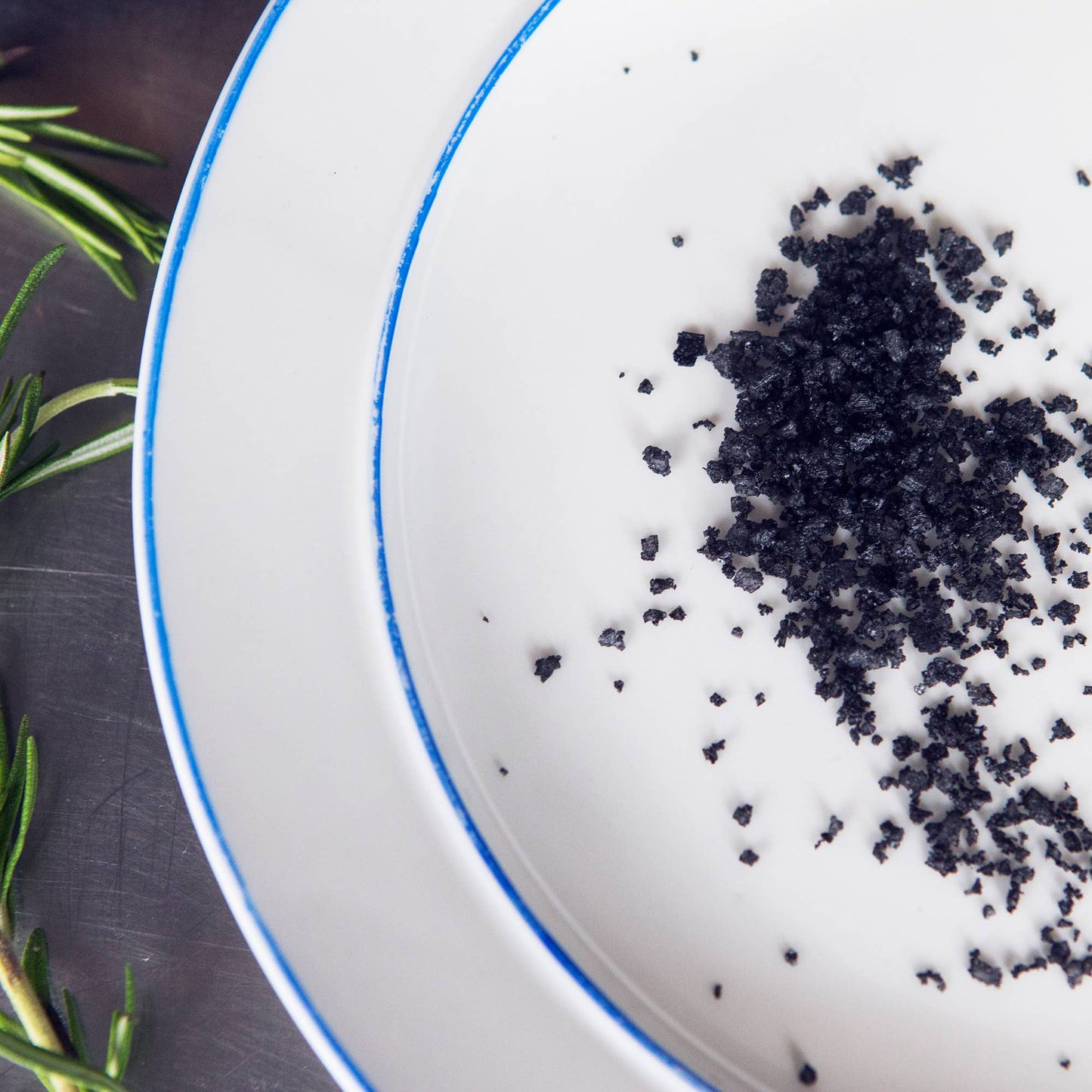 White plate with black crumbly salt on a dark surface