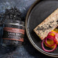 Plated dish with salmon and vegetables next to a jar of Saltwerk Lava Salt on a dark surface.